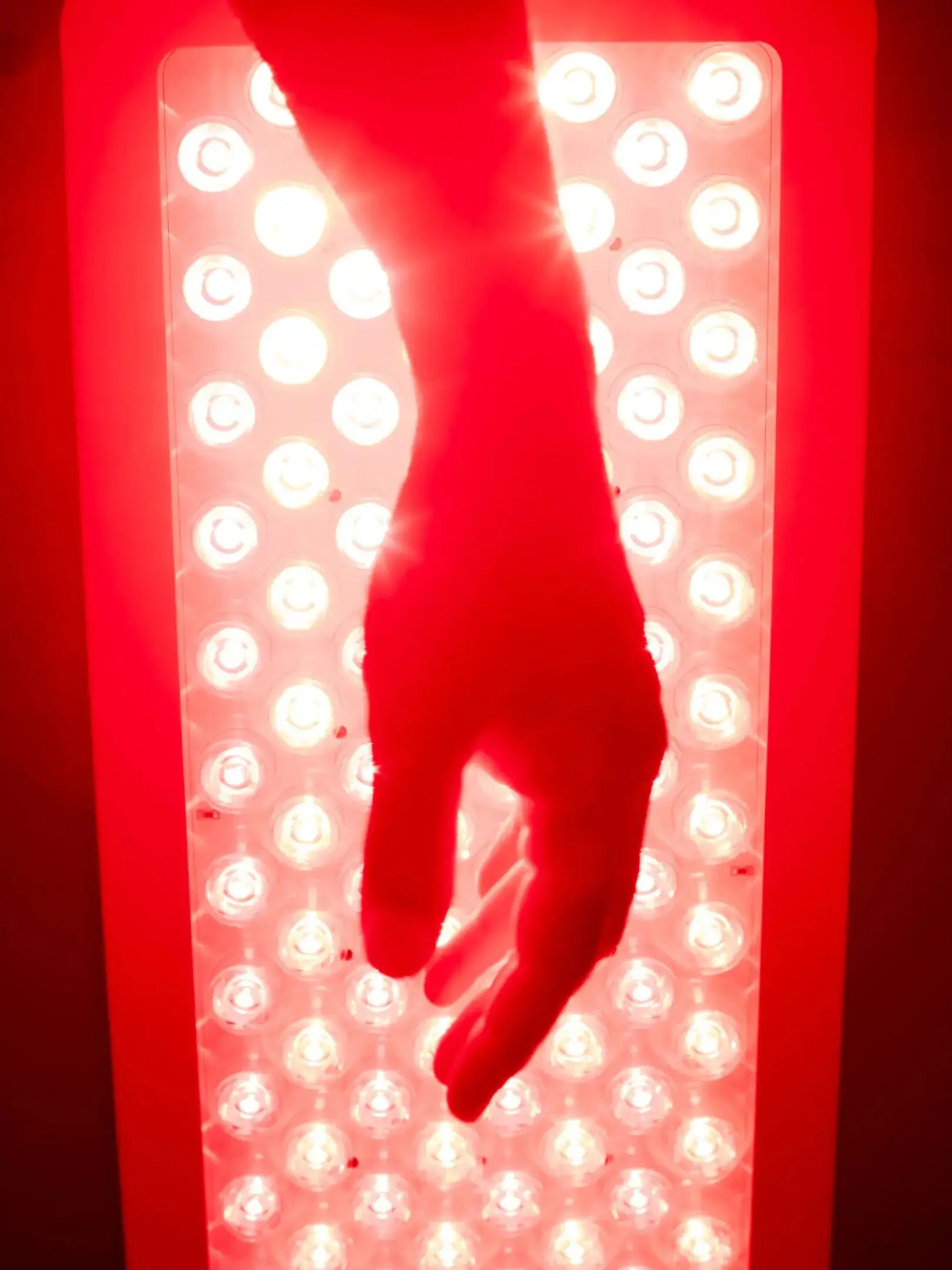 Hand silhouetted over red LED light panel