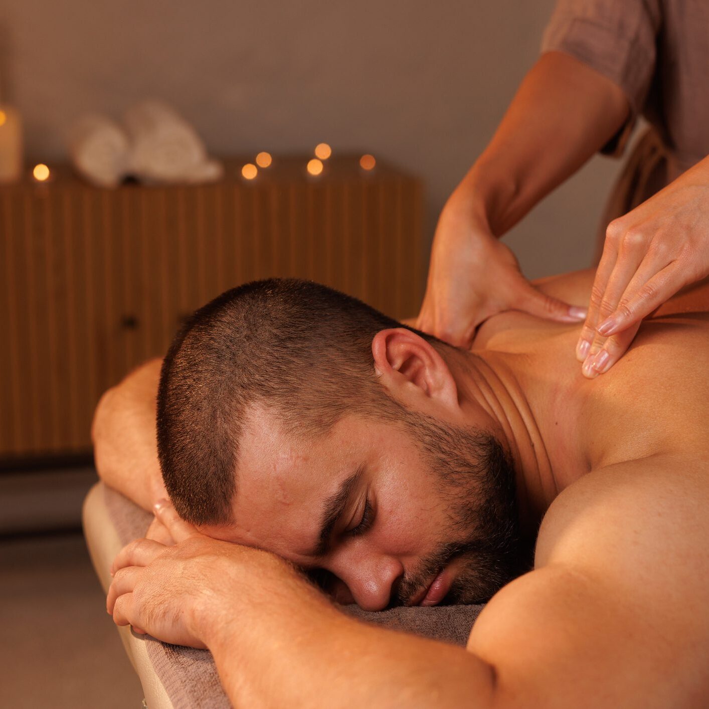 Relaxing neck massage, healthy massaging rehab concept. Close-up hands of woman masseur doing wellness medical relaxing massage for male patient in dark medical office in shadow. Copy ad text space